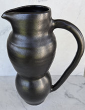 Load image into Gallery viewer, Matte black pitcher with a glossy interior rim, a curved handle, and a two-tiered bulbous body, shown from the front.