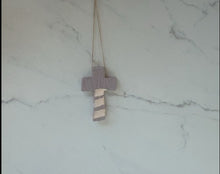 Load image into Gallery viewer, A rustic wooden cross hangs on a string against, marble-patterned background. The cross has 3 white stripes on bottom section of cross.
