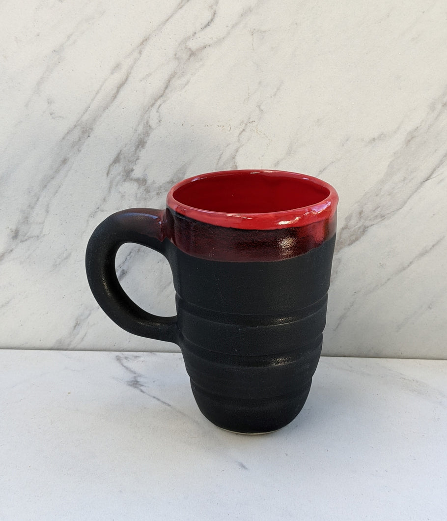 Black mug with red glaze dripping from lip of mug.